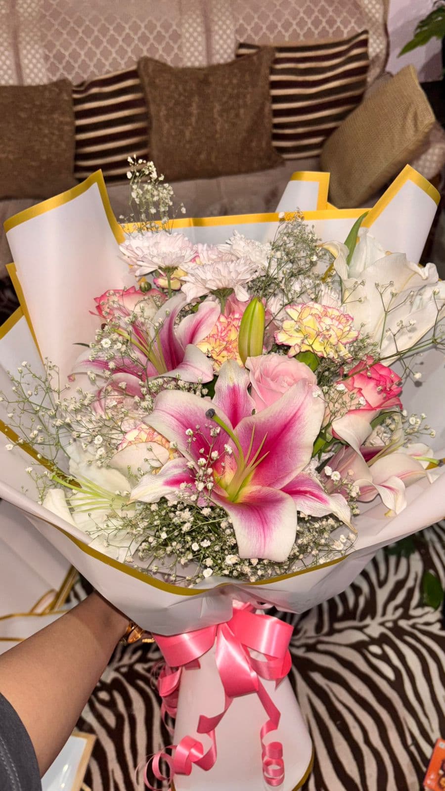 A recipient holding a wrapped bouquet of pink lilies and roses at home.