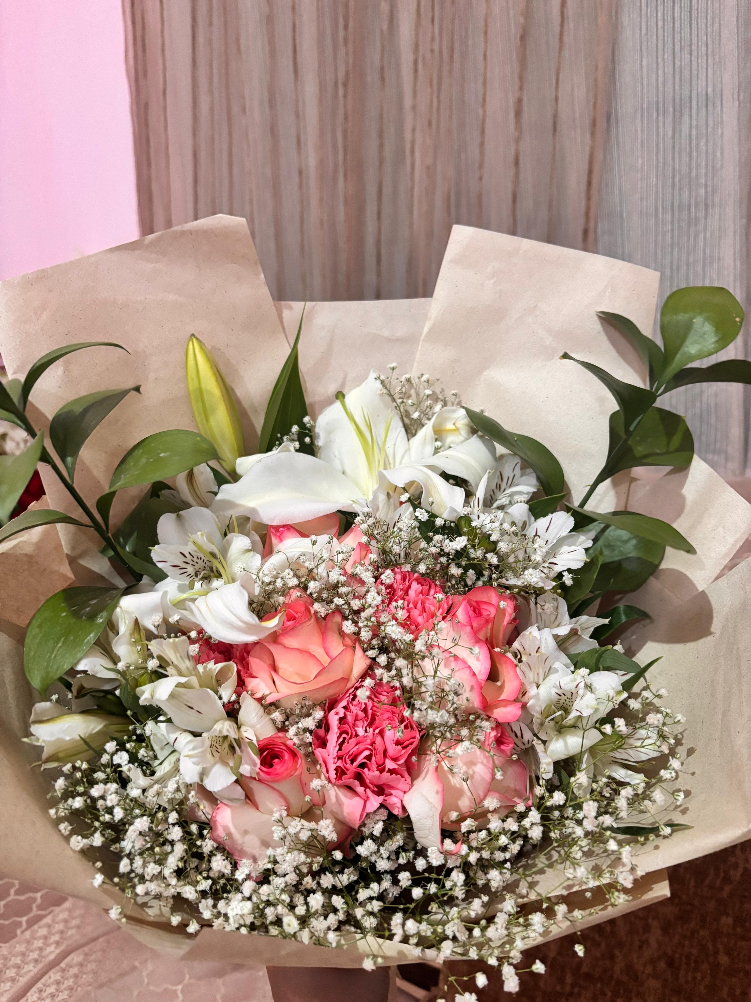 A Little Token signature bouquet of pink roses, white lilies and baby's breath in kraft paper.